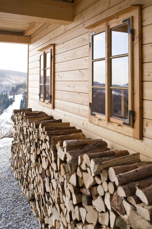 Gestapeltes Brennholz an der Holzfassade, Blick ins verschneite Tal